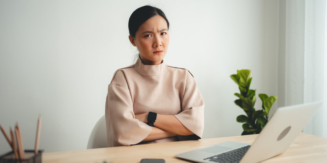 Asian Woman Using Laptop Suffering From Problem With Work Or Financial, Looking To Camera.